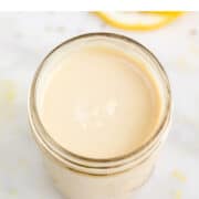 Jar with lemon tahini dressing and lemon slices in the background.