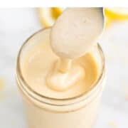 Jar of lemon tahini dressing being drizzled with a spoon.