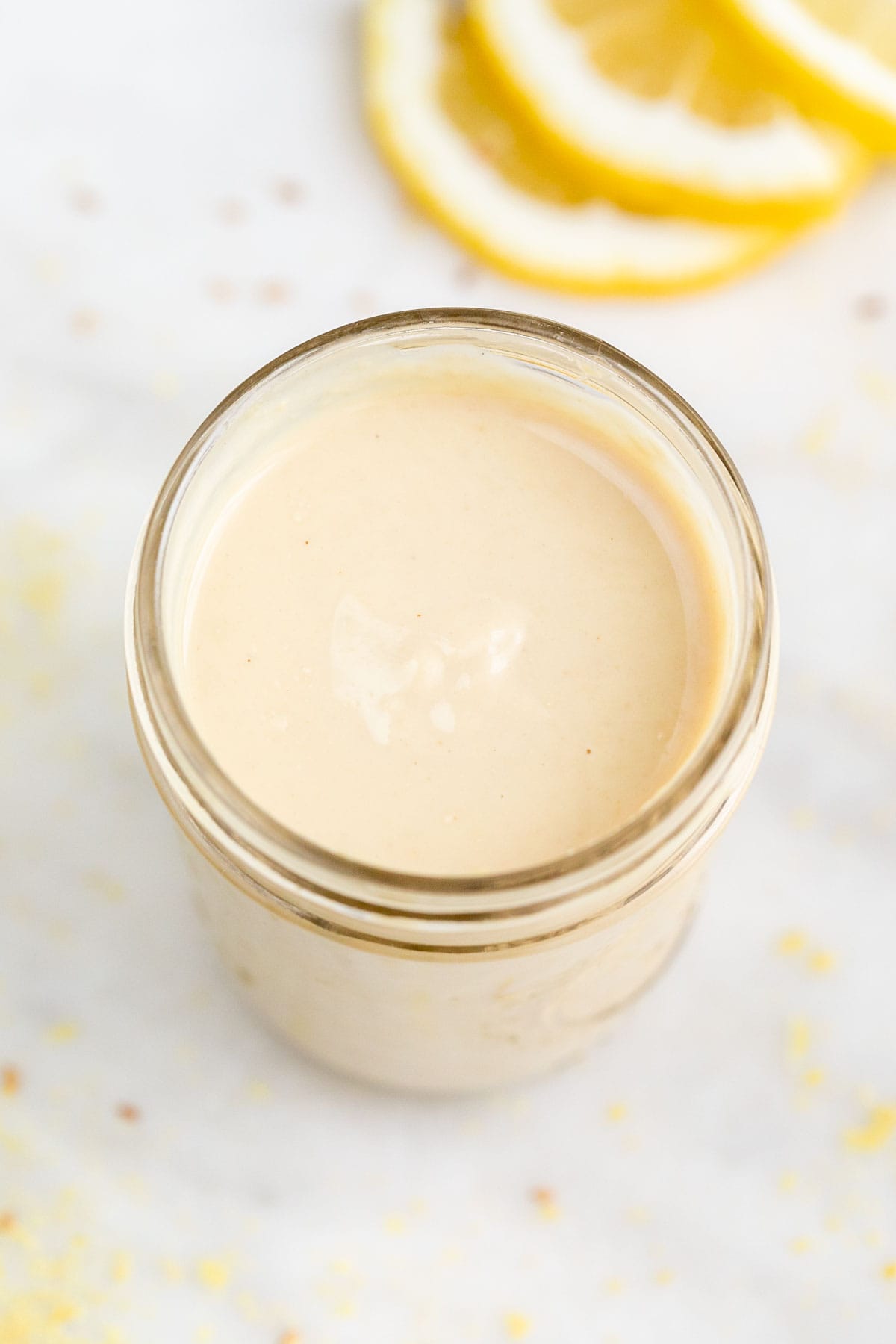Jar containing lemon tahini dressing with lemon slices in the background.