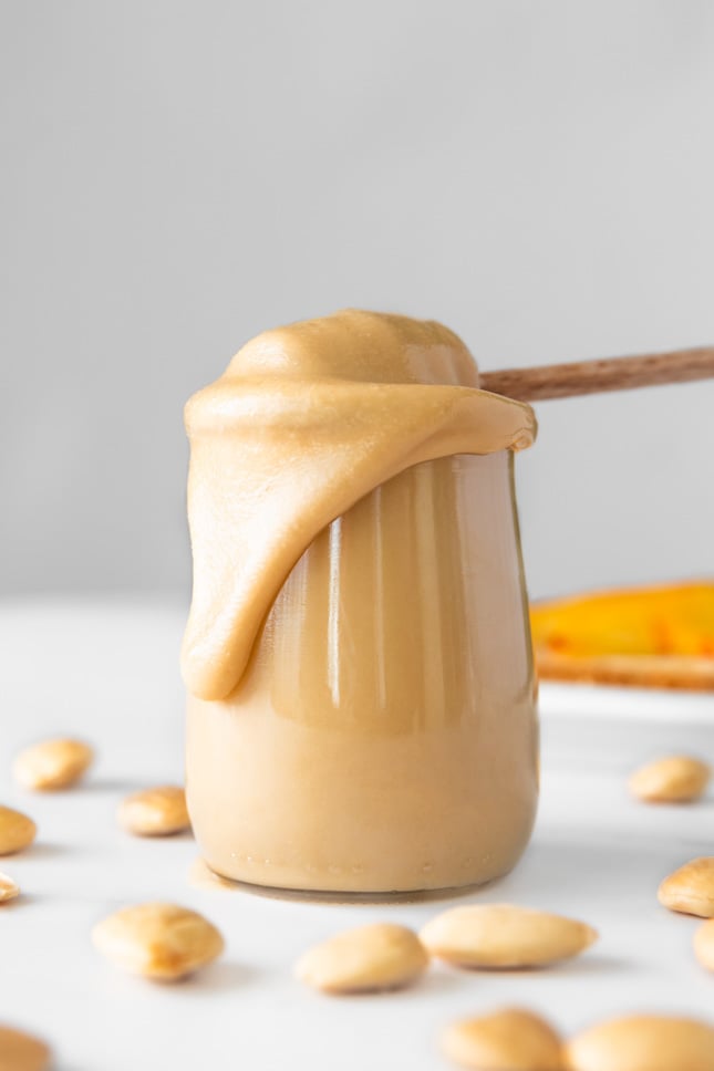 Side shot of a glass of creamy almond butter with a honey spoon in it