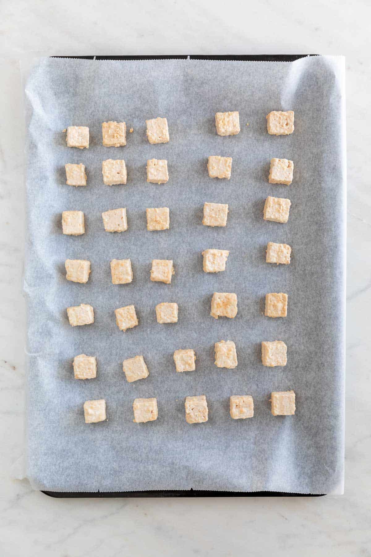 Tofu cubes onto a lined baking sheet before baking.