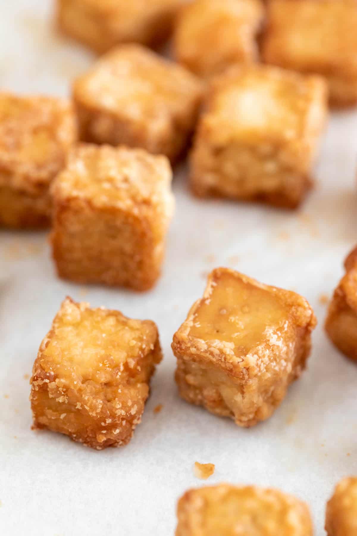 Several baked tofu cubes onto a lined baking sheet.