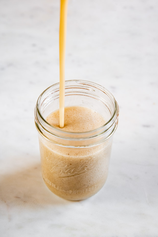A picture of someone pouring some banana milk into a jar
