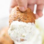 A hand with a beer-battered vegan fish stick with some vegan tartar sauce and with a heading.