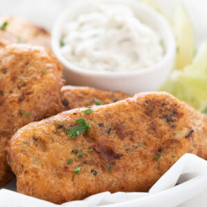 Square photo of a dish with beer-battered vegan fish sticks garnished with chopped parsley.