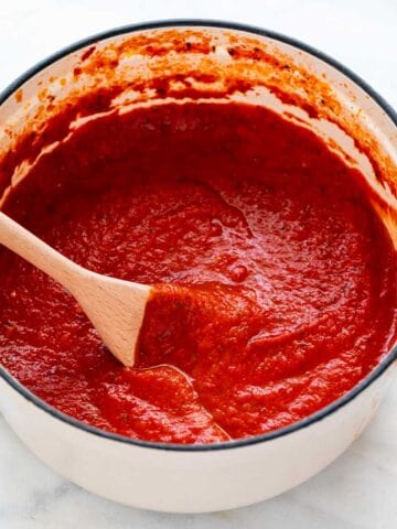 Homemade marinara sauce in a large pot stirring with a spoon.