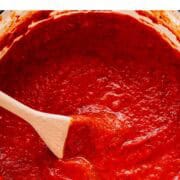 Homemade marinara sauce in a large pot with a wooden spoon.
