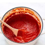 Homemade marinara sauce in a pot with a spoon.