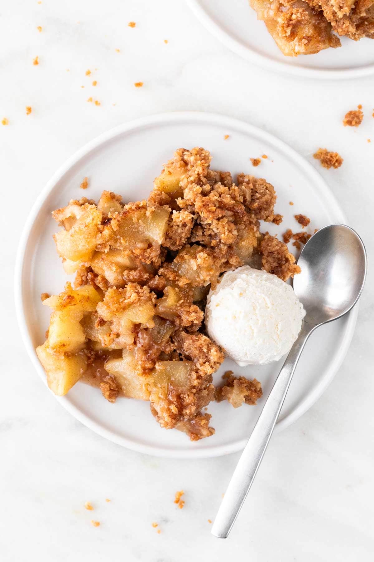 Vegan apple crisp with vegan vanilla ice cream and a spoon on a plate.