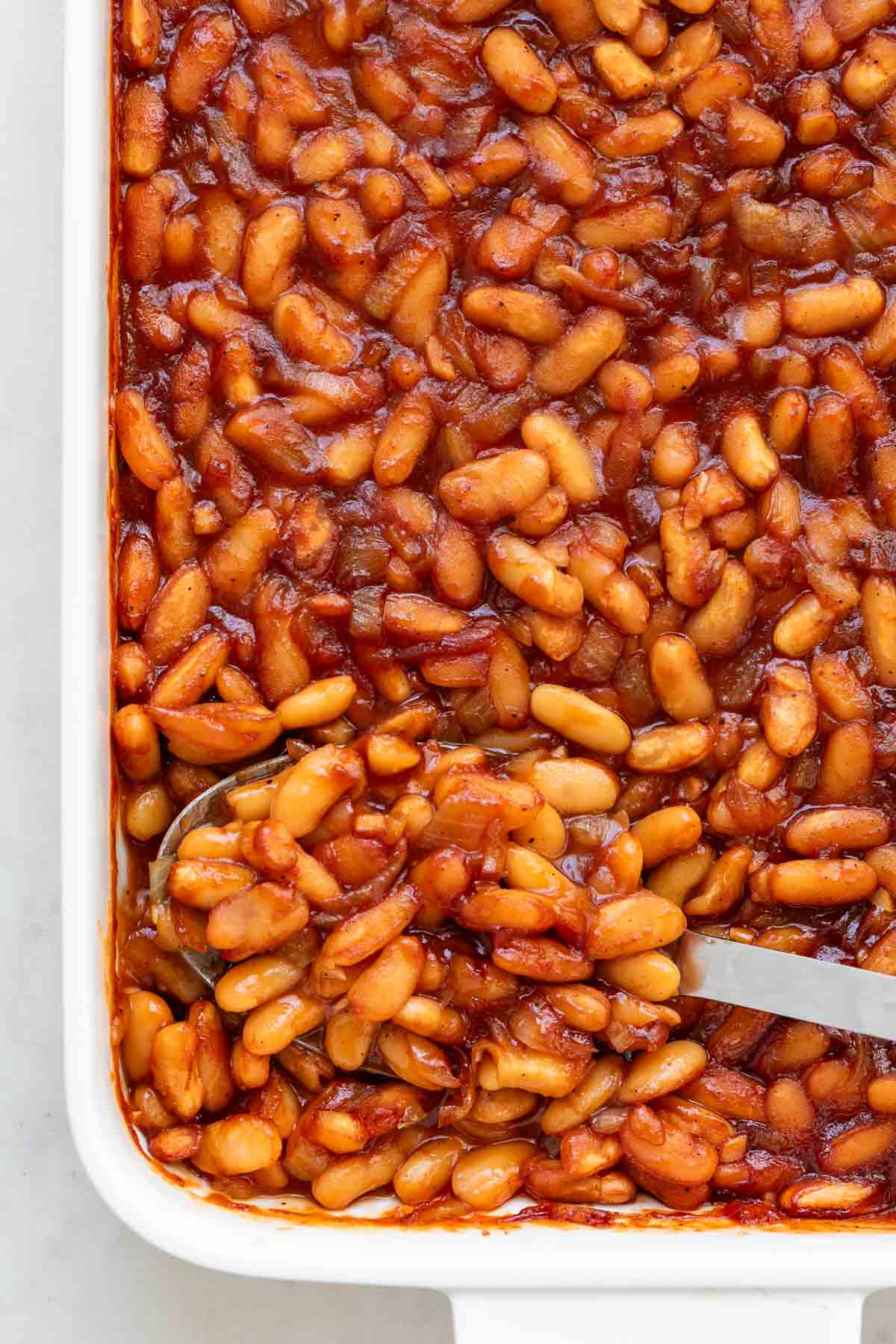 Vegan baked beans in casserole dish with serving spoon.