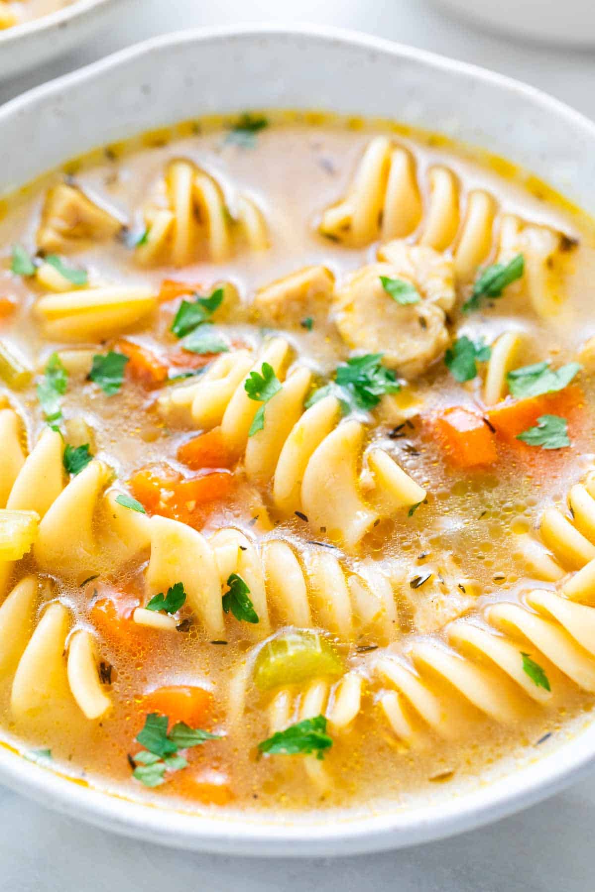 Vegan chicken noodle soup in a shallow dish garnished with parsley.