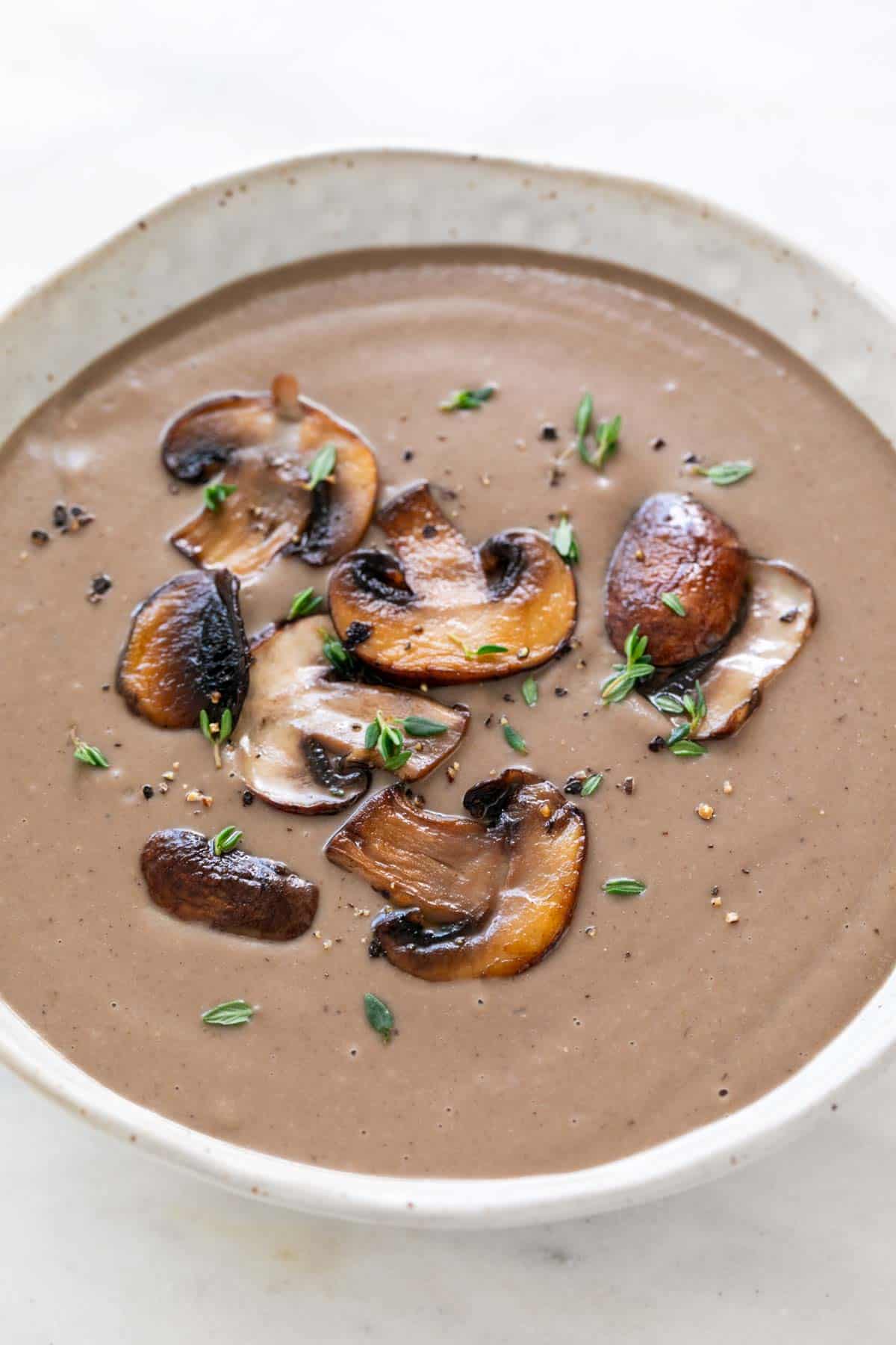 Bowl of vegan cream of mushroom soup topped with sautéed mushrooms, fresh thyme, and black pepper.