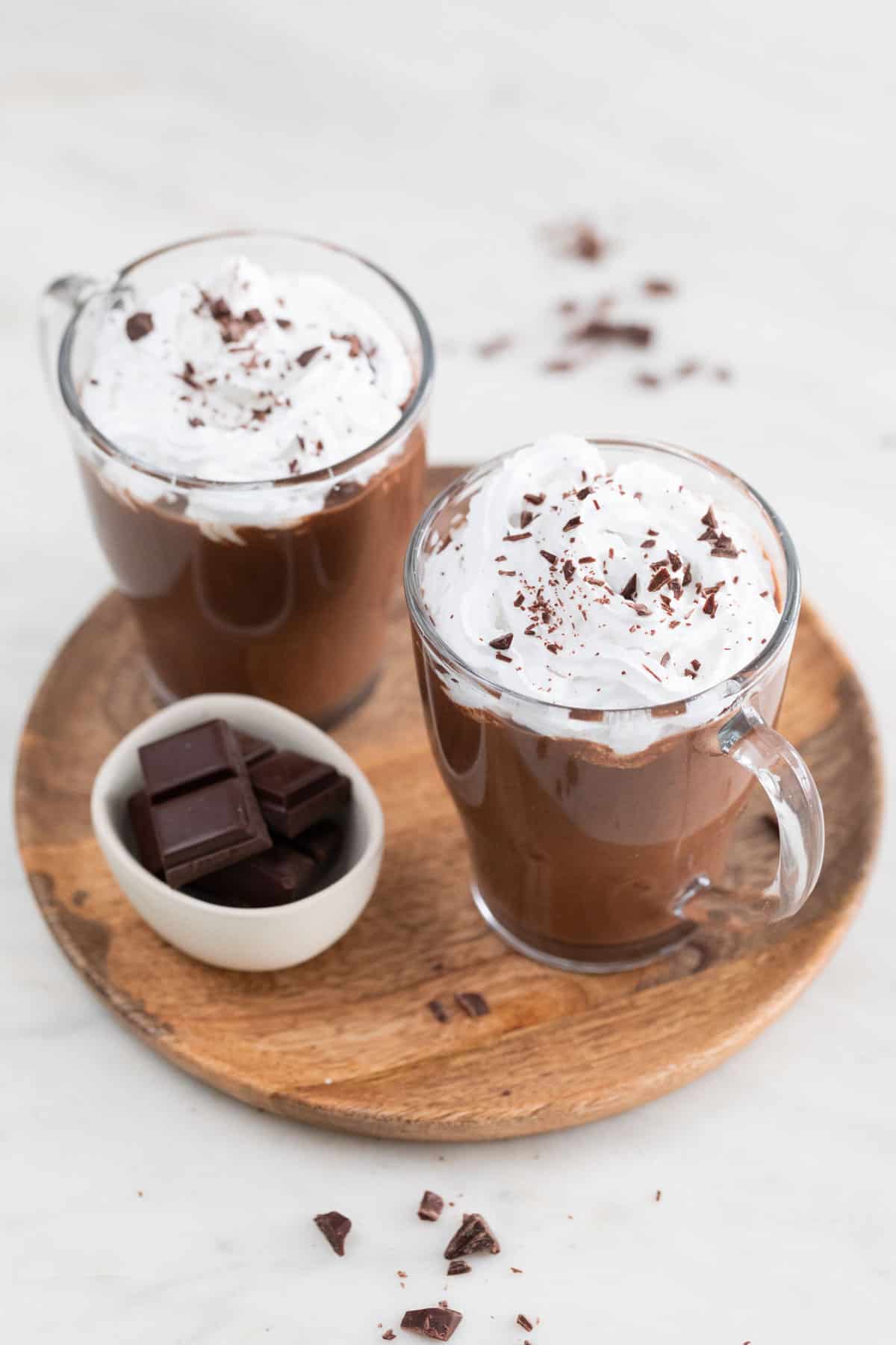 Two jars of vegan hot chocolate topped with vegan whipped cream and chopped dark chocolate.