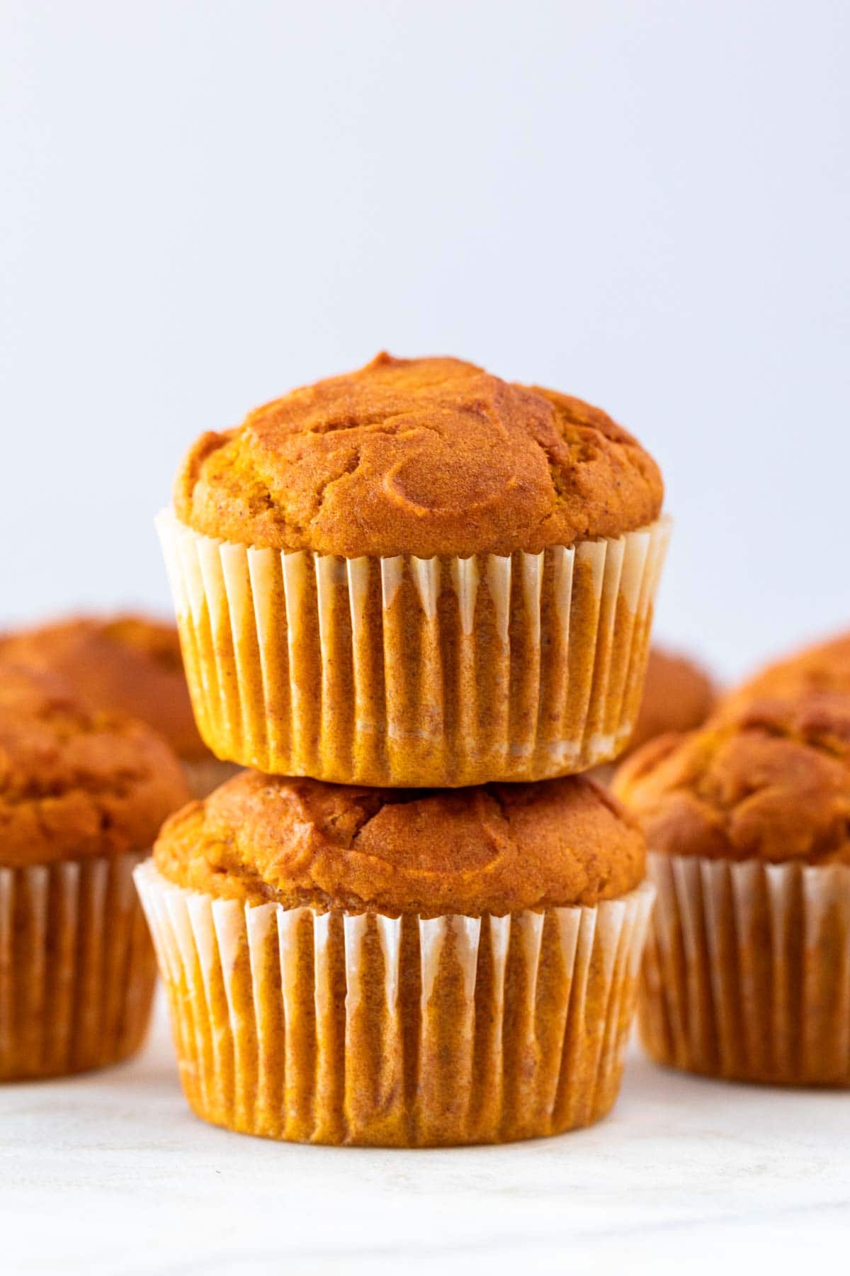 Vegan pumpkin muffins arranged in a stack, surrounded by additional muffins.