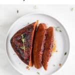 Slices of vegan steak on a white plate, with a sprinkle of fresh thyme.