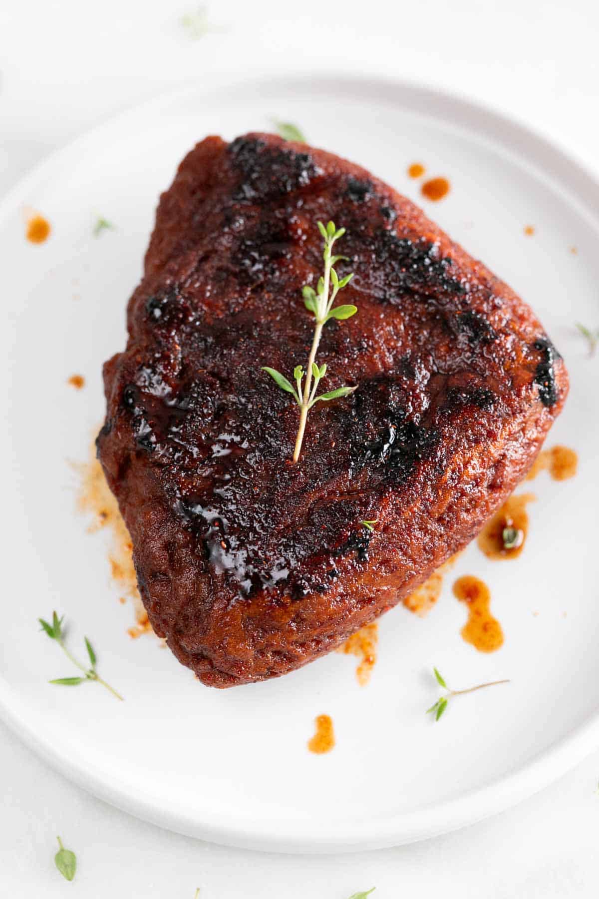 Vegan steak on a white plate with fresh thyme on top.