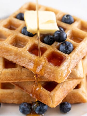 A tower of fluffy vegan waffles topped with blueberries, vegan butter, and maple syrup.