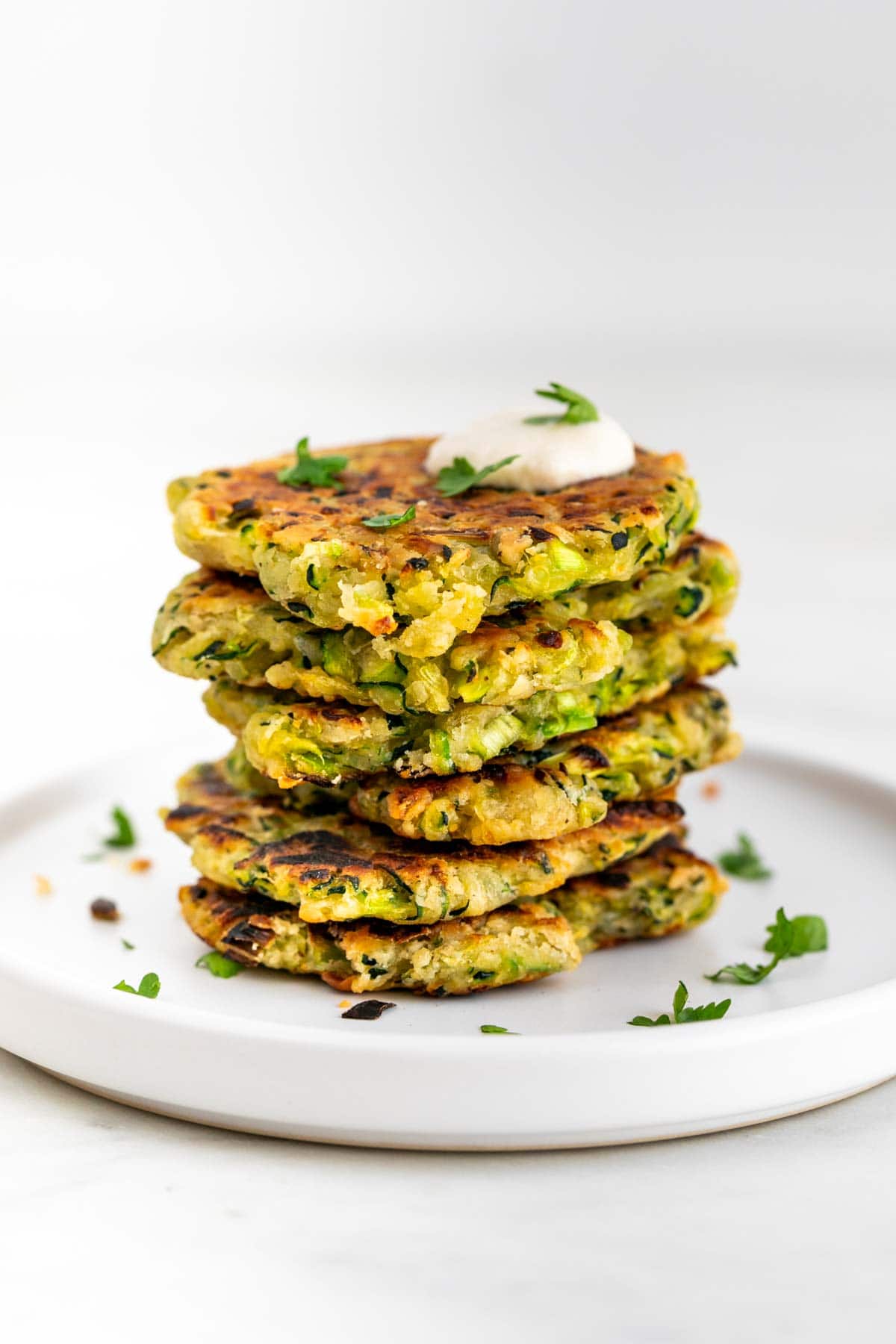 Vegan zucchini fritters served with a dollop of vegan sour cream and topped with parsley.