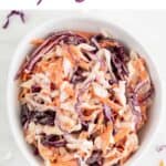 White bowl with vegan coleslaw surrounded by vegetables.