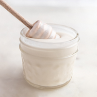 Square photo of a glass of coconut butter with a honey dipper in it