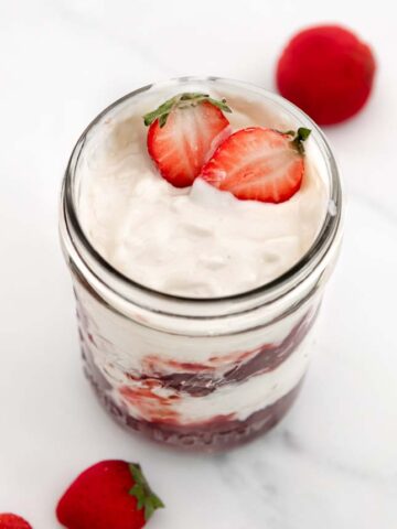 Photo of a glass jar of coconut yogurt with some strawberries