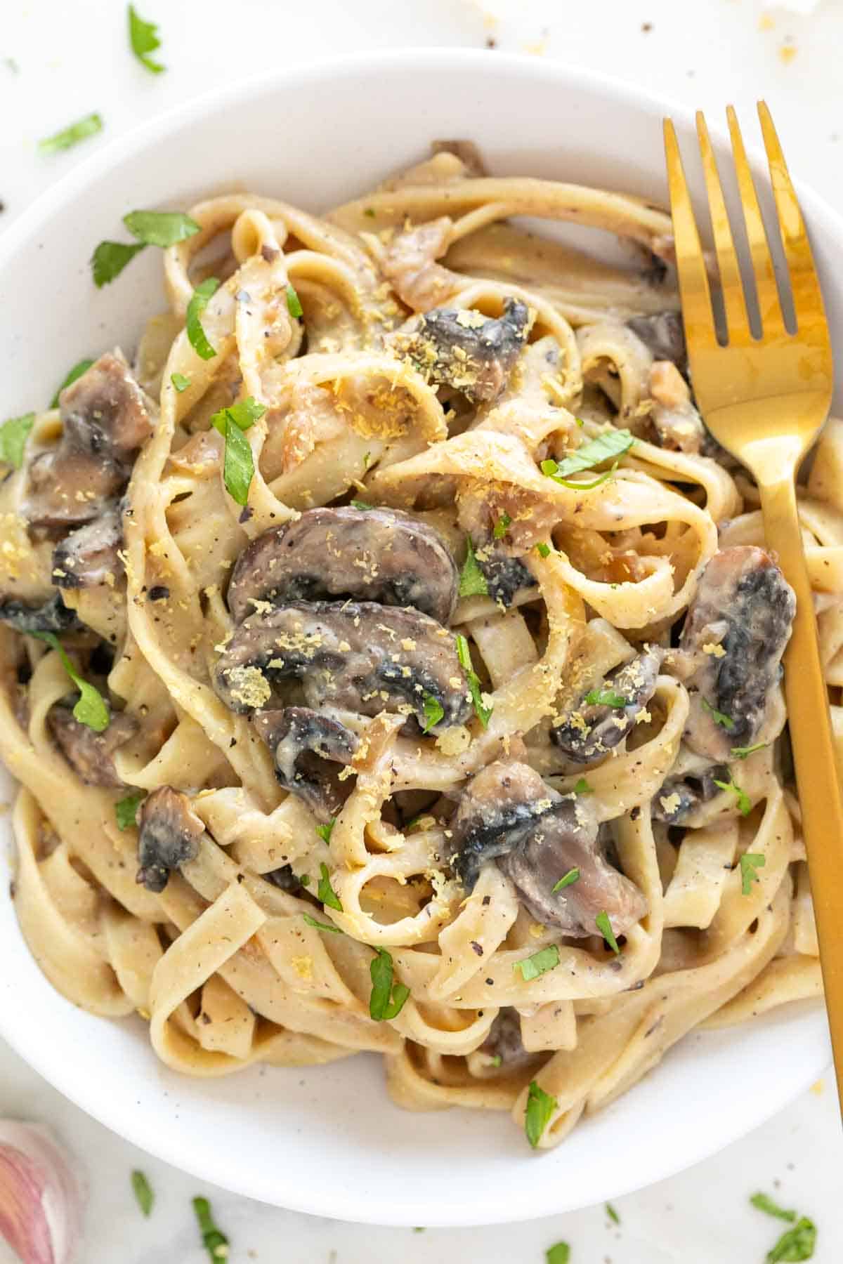 Golden fork over a plate of vegan mushroom pasta.