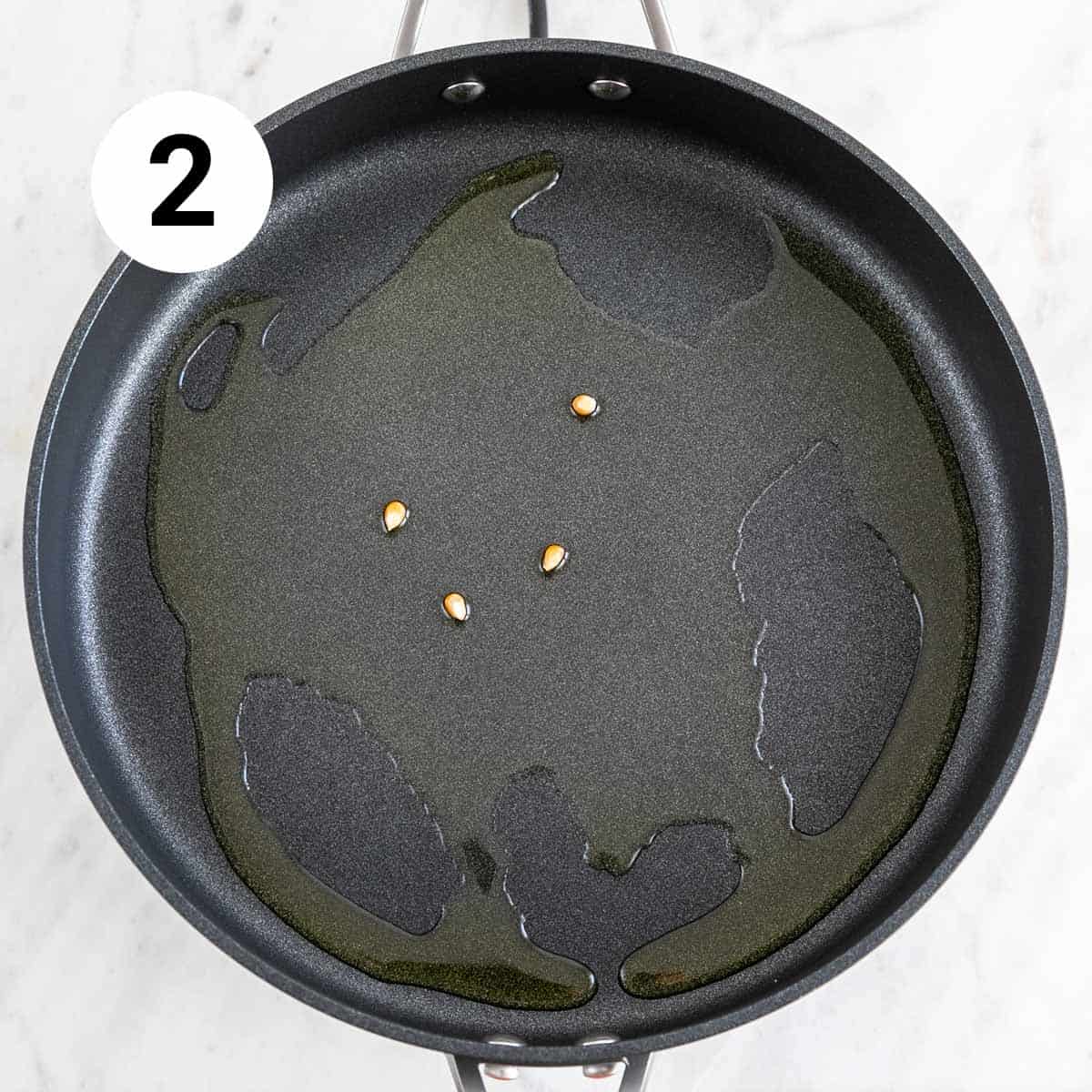 Skillet with extra virgin olive oil and four popcorn kernels.