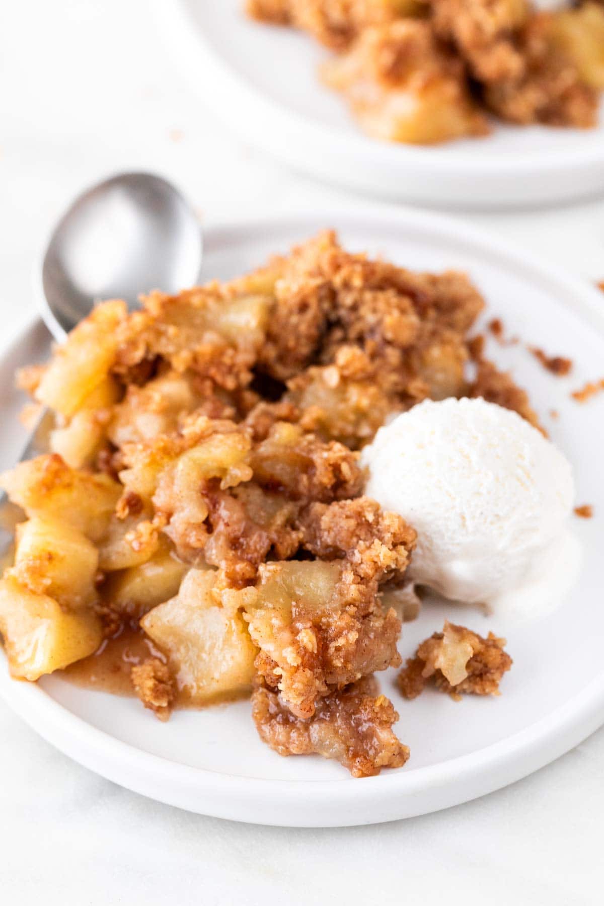 Plate of vegan apple crisp with vegan vanilla ice cream and a spoon.