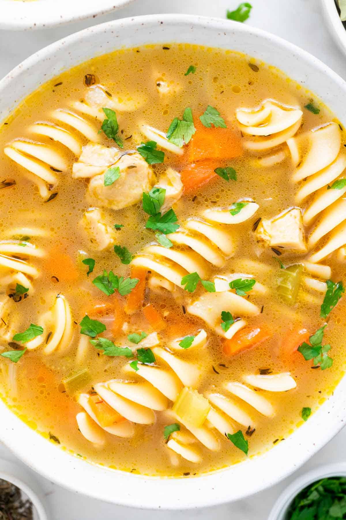 Vegan chicken noodle soup served in a shallow dish with parsley on top.