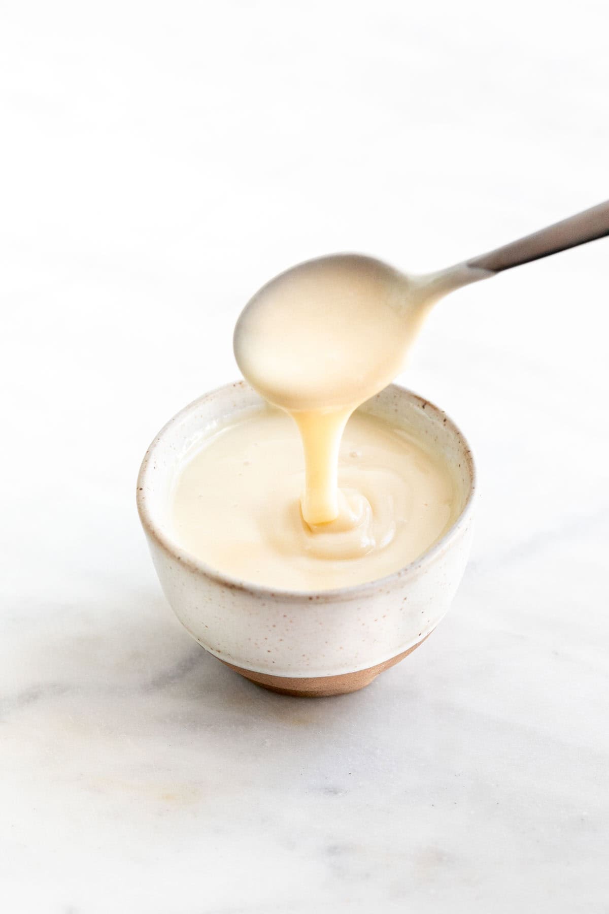Spoon scooping vegan sweetened condensed milk from a bowl.