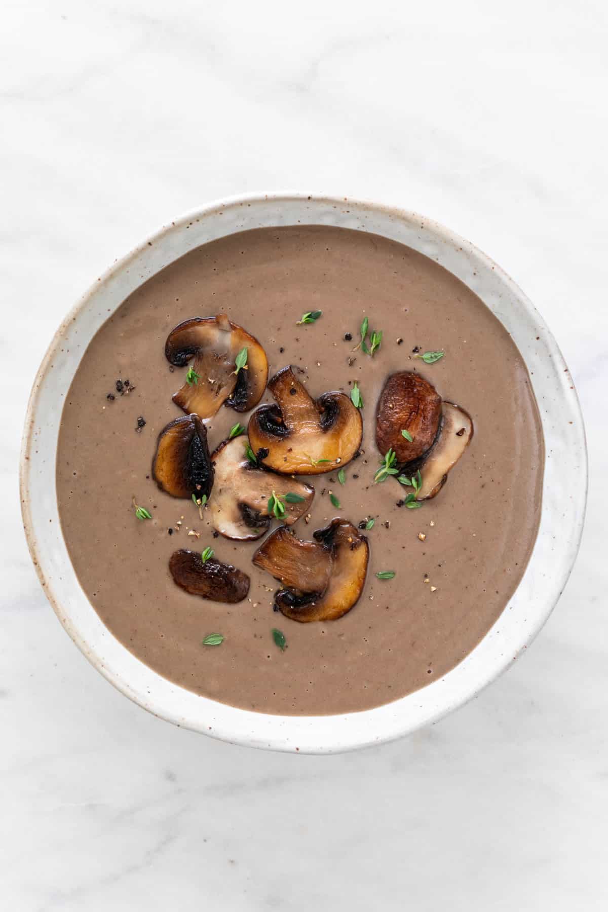 Vegan cream of mushroom soup in a bowl with sautéed mushrooms, thyme, and black pepper garnish.