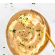 Mashed potatoes and vegan gravy in a bowl, topped with fresh parsley and a serving spoon.
