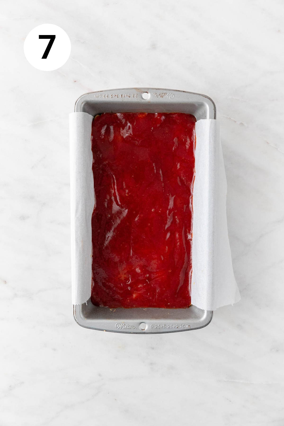 Vegan lentil loaf mixture in a lined loaf pan covered with the glaze before baking.