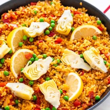 Vegan paella in a paella pan with lemon wedges on top.