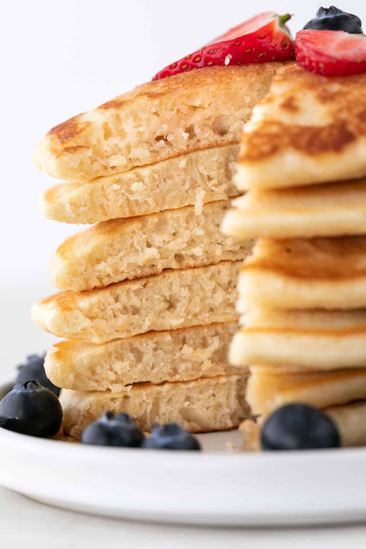 Stack of sliced vegan pancakes topped with fresh strawberries and blueberries.