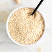White bowl of vegan Parmesan cheese with a serving spoon.