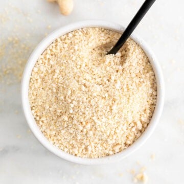 White bowl of vegan Parmesan cheese with a serving spoon.