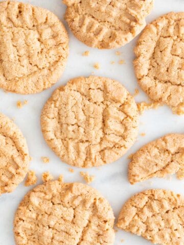 Lots of vegan peanut butter cookies on a marble slab.