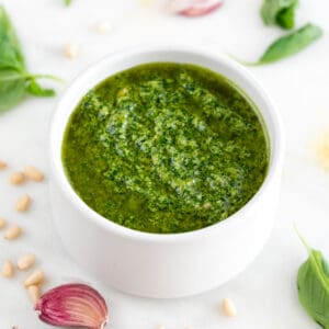 White bowl of vegan pesto with ingredients in the background.