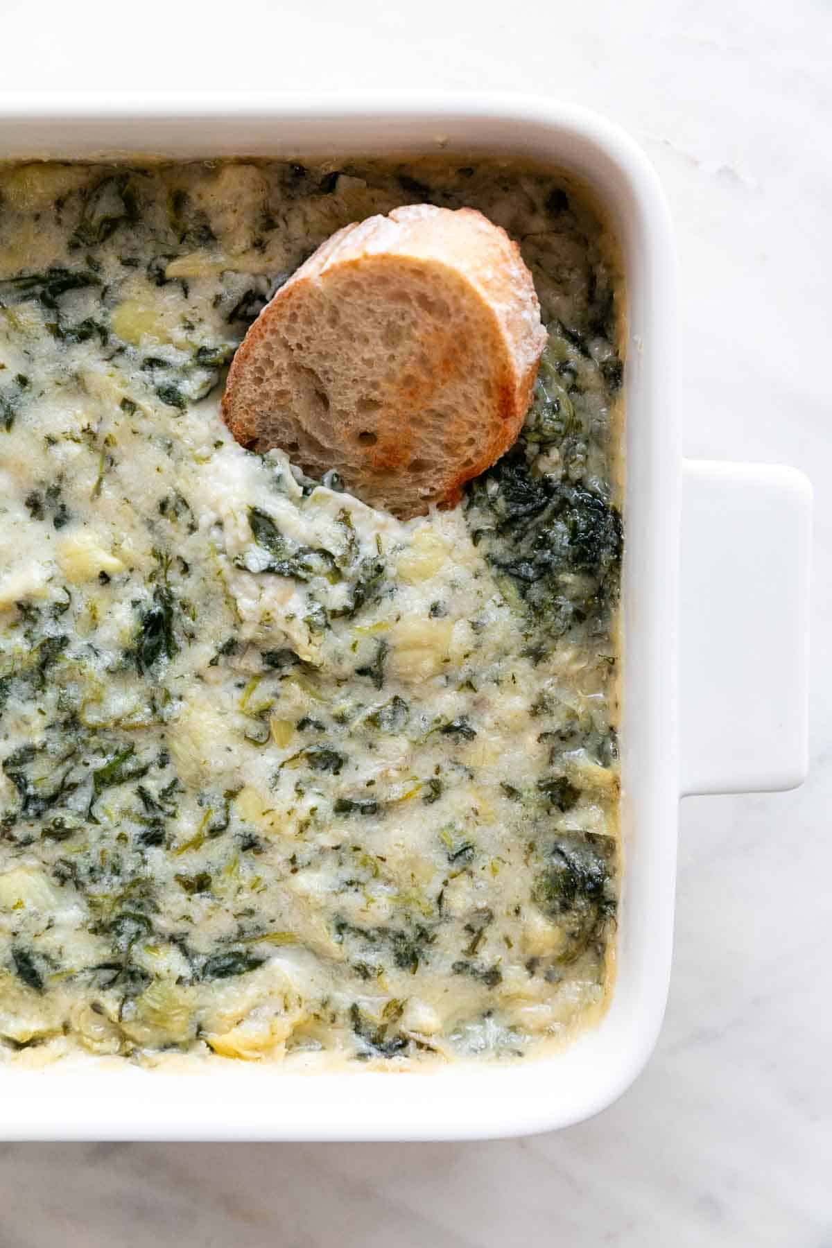 Baking dish with vegan spinach dip and a slice of bread.