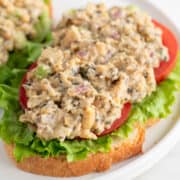 Vegan tuna on a slice of bread, with lettuce and tomato slices, on a white plate.