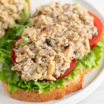 Vegan tuna on a slice of bread, with lettuce and tomato slices, on a white plate.