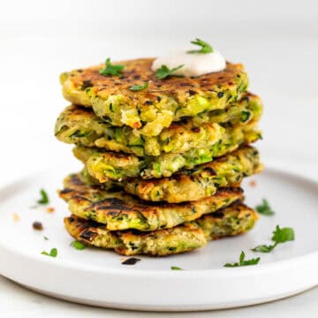 Vegan zucchini fritters served with a dollop of vegan sour cream and topped with parsley.