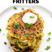 Vegan zucchini fritters served on a plate with a dollop of vegan sour cream and parsley.