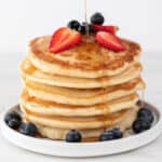 Vegan pancakes heaped with strawberries, blueberries, and maple syrup drizzle.