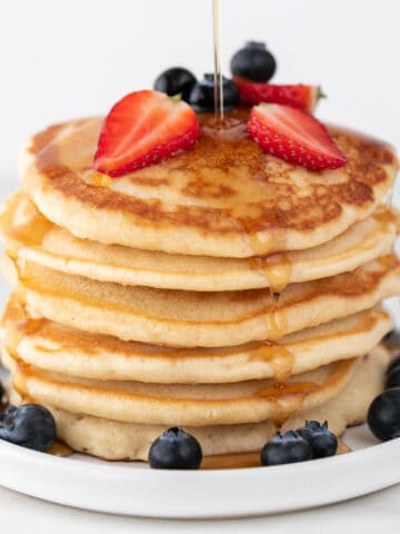Vegan pancakes heaped with strawberries, blueberries, and maple syrup drizzle.
