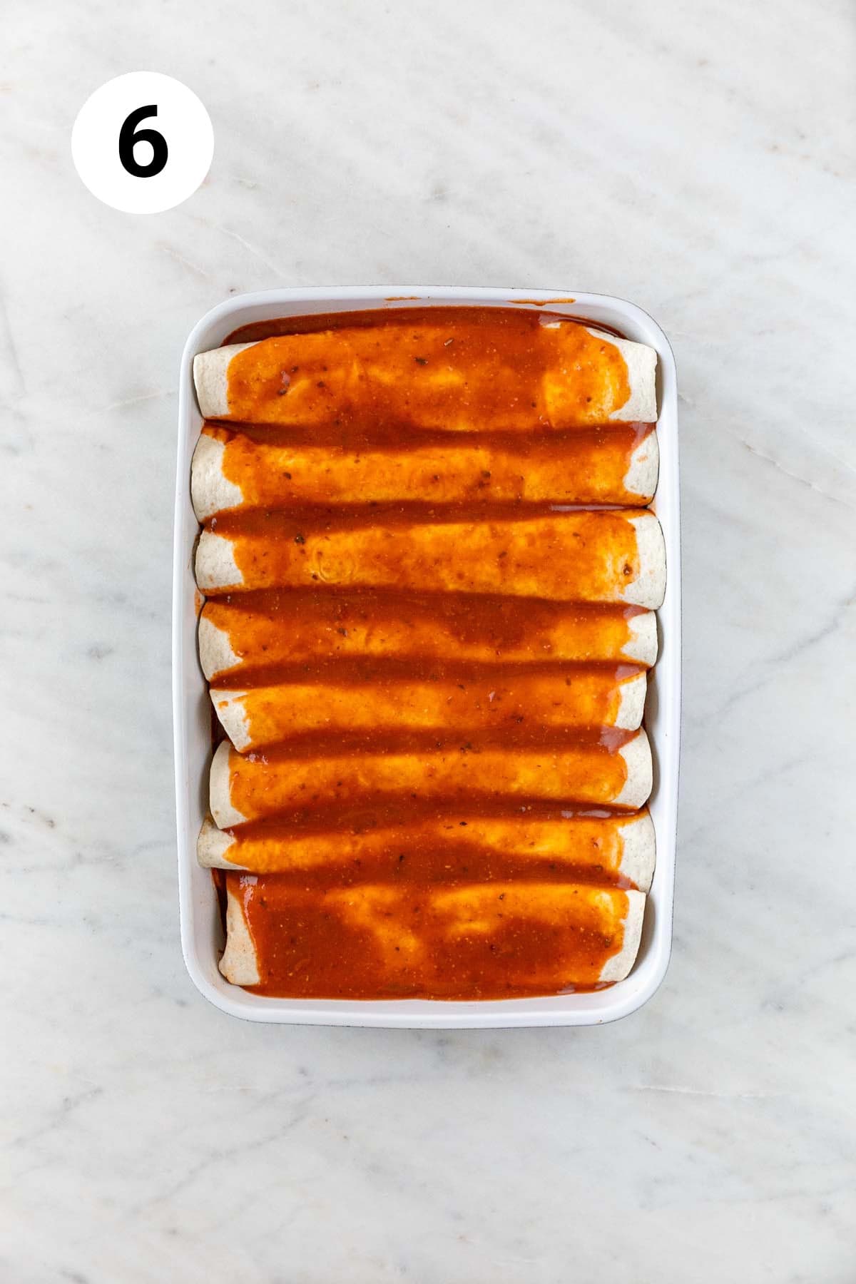 Red enchilada sauce over a baking dish of enchiladas.