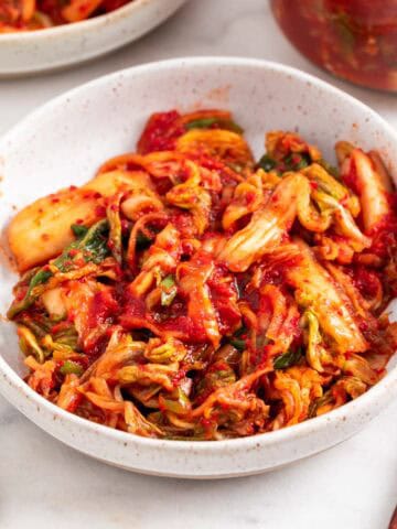 Vegan kimchi in two shallow dishes and in a jar.