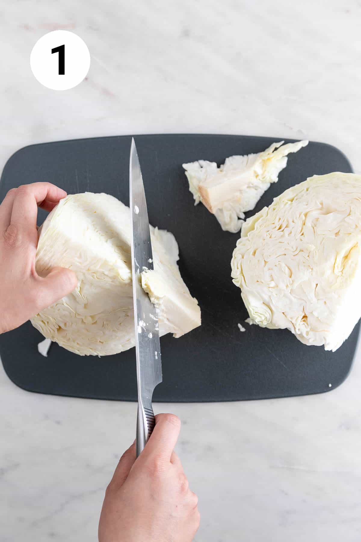 Hands removing the tough core from a green cabbage on a cutting board.