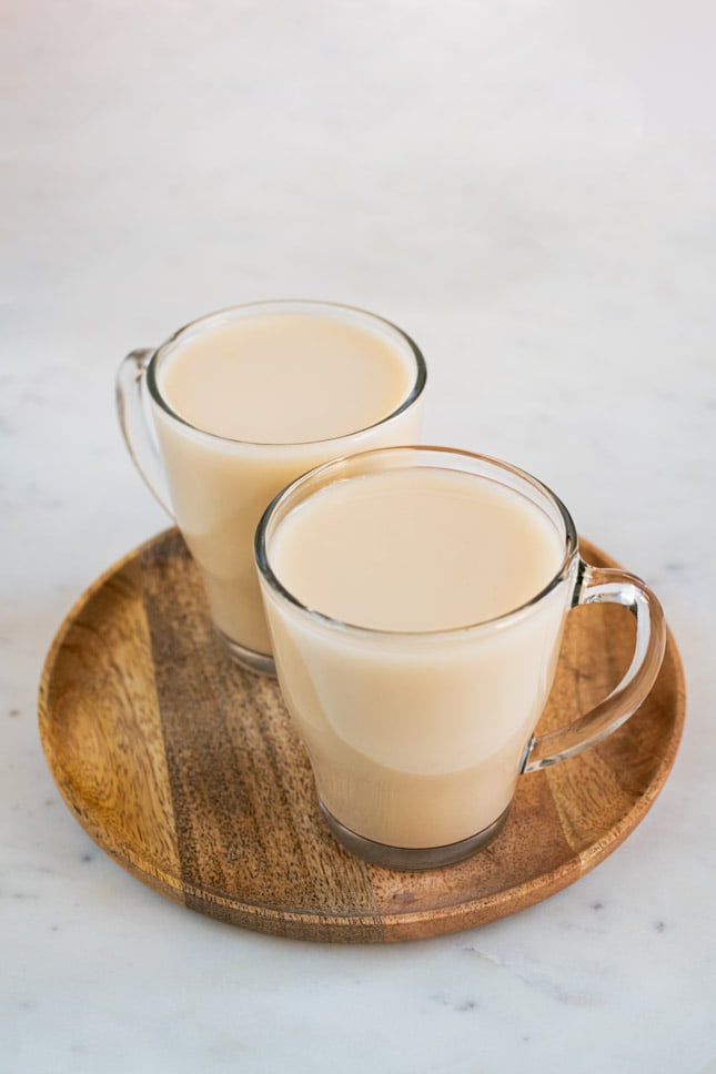 A picture of 2 mugs with homemade oat milk onto a wooden tray